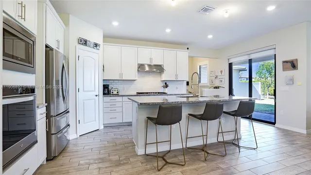 a kitchen with stainless steel appliances granite countertop a stove a sink a refrigerator a microwave oven with white cabinets and wooden floor