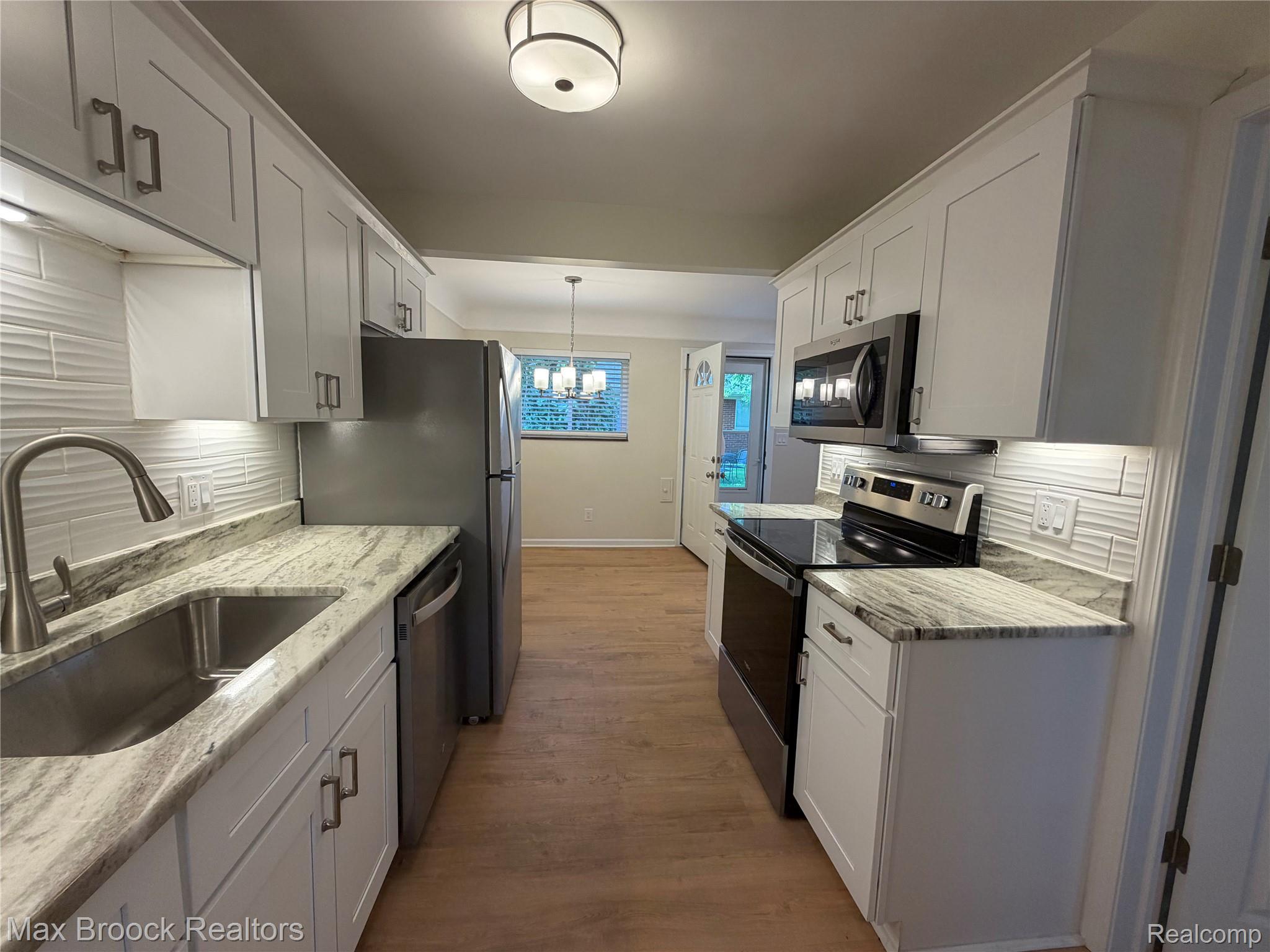 3875 Devon Road, Unit # 9 Royal Oak, MI 48073 - Photo 4 of 17 Modern kitchen featuring white shaker cabinetry, stainless steel appliances, light-toned countertops, and a textured tile backsplash