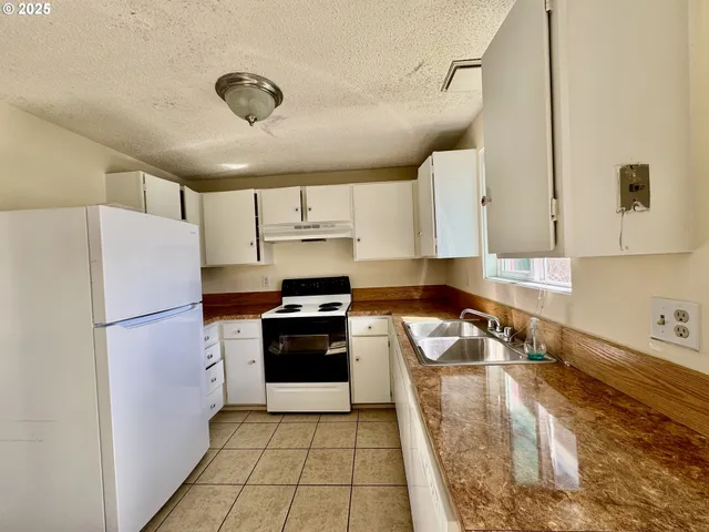 a kitchen with granite countertop a refrigerator a sink and white cabinets