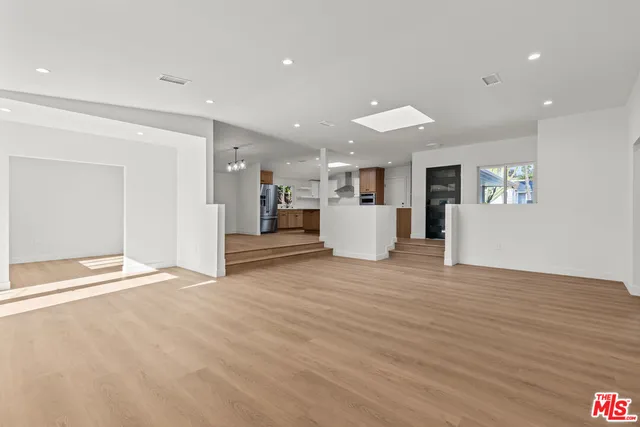 a view of an empty room with wooden floor and kitchen view