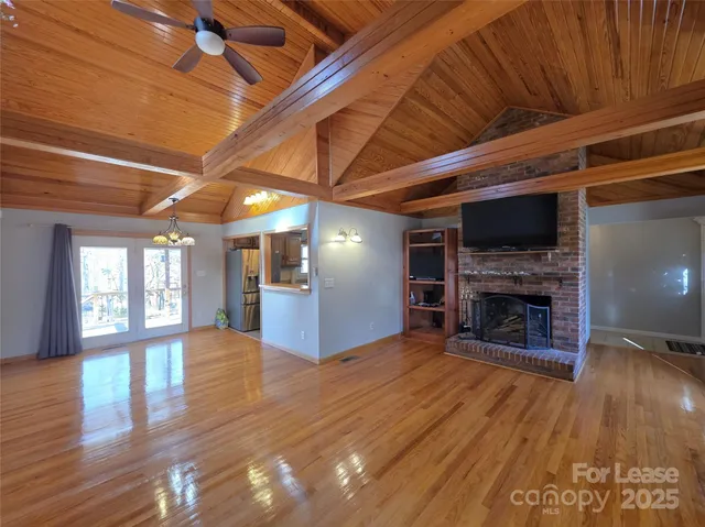 a view of an empty room with wooden floor a fireplace and a window