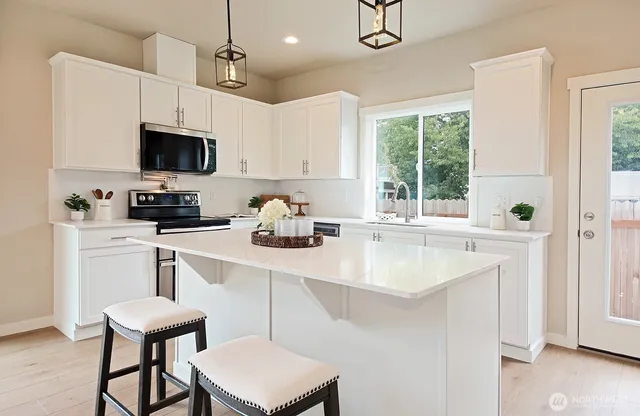 a kitchen with stainless steel appliances a sink a stove a microwave a refrigerator a dining table and chairs with wooden floor