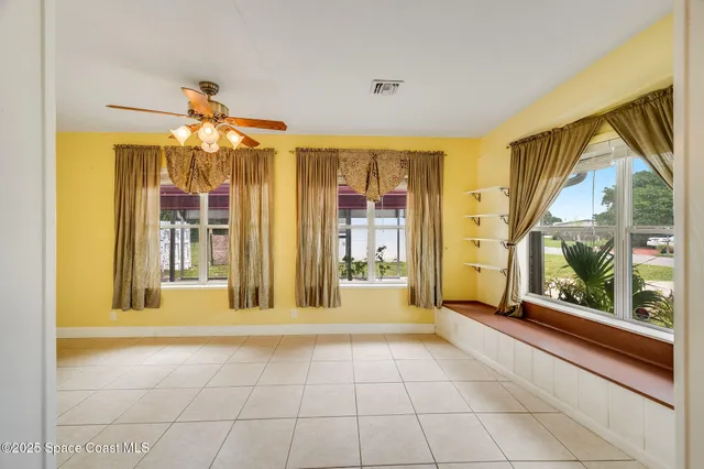an empty room with chandelier fan and windows