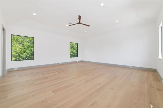 an empty room with wooden floor ceiling fan and windows