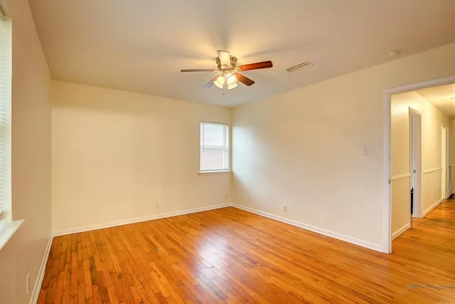 an empty room with wooden floor fan and windows