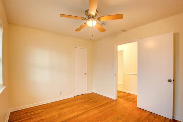 a view of an empty room with wooden floor and a ceiling fan