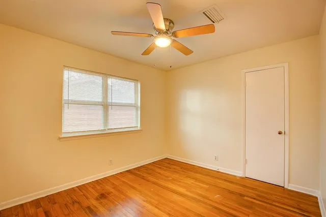 an empty room with wooden floor fan and windows