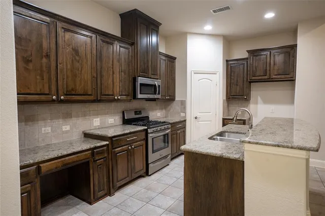 a kitchen with kitchen island granite countertop a sink dishwasher stove and refrigerator with wooden cabinets