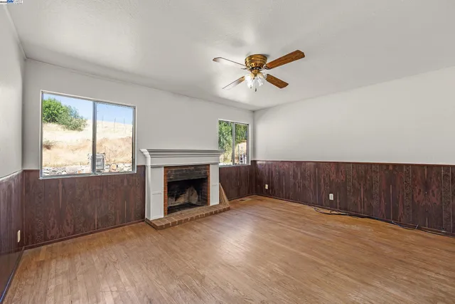 a view of an empty room with wooden floor fireplace and a window