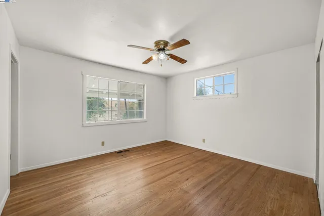 an empty room with wooden floor ceiling fan and windows