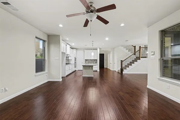 a view of an empty room with wooden floor a ceiling fan and windows