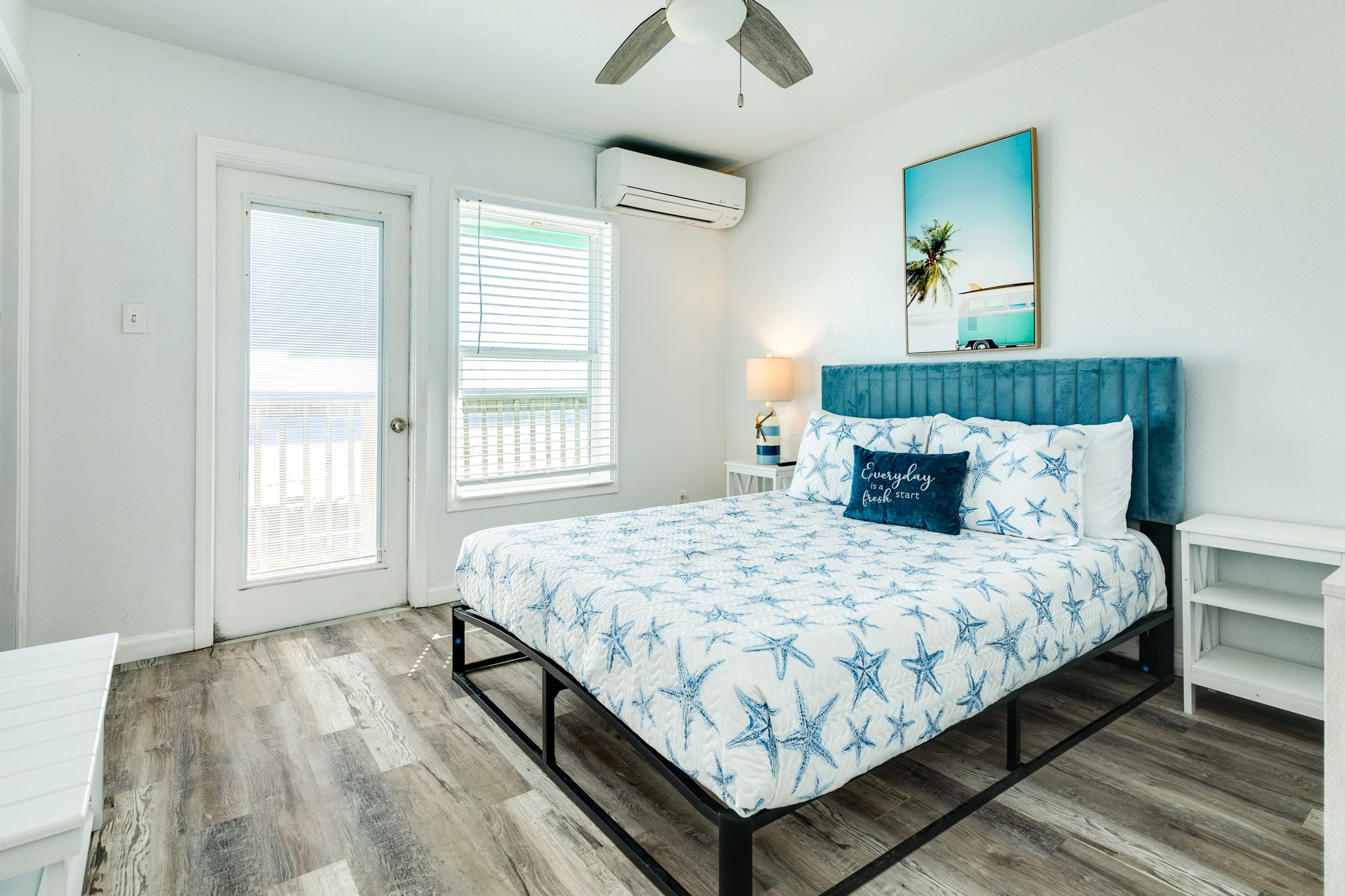 101 Pelican Place, Unit 7 Freeport, TX 77541 - Photo 23 of 44 This bright bedroom features a modern design with a starfish-themed bedspread, wood-style flooring, and a cozy blue headboard. It includes a ceiling fan, air conditioning, and access to a private balcony through a glass door, perfect for enjoying natural light and fresh air.