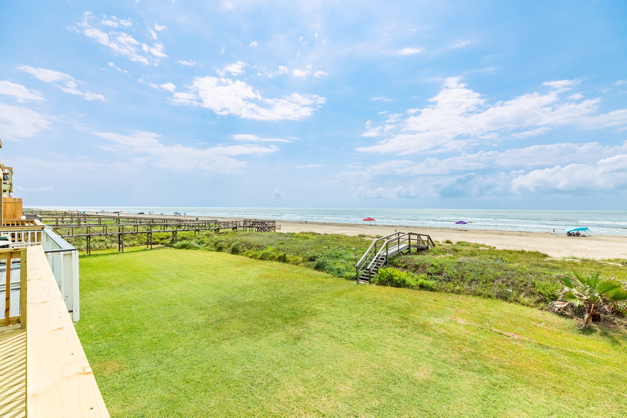 101 Pelican Place, Unit 7 Freeport, TX 77541 - Photo 28 of 44 This photo showcases a beachfront property with a spacious grassy yard leading to a wooden walkway and direct access to a sandy beach. The view features a clear blue sky and ocean, perfect for seaside living.