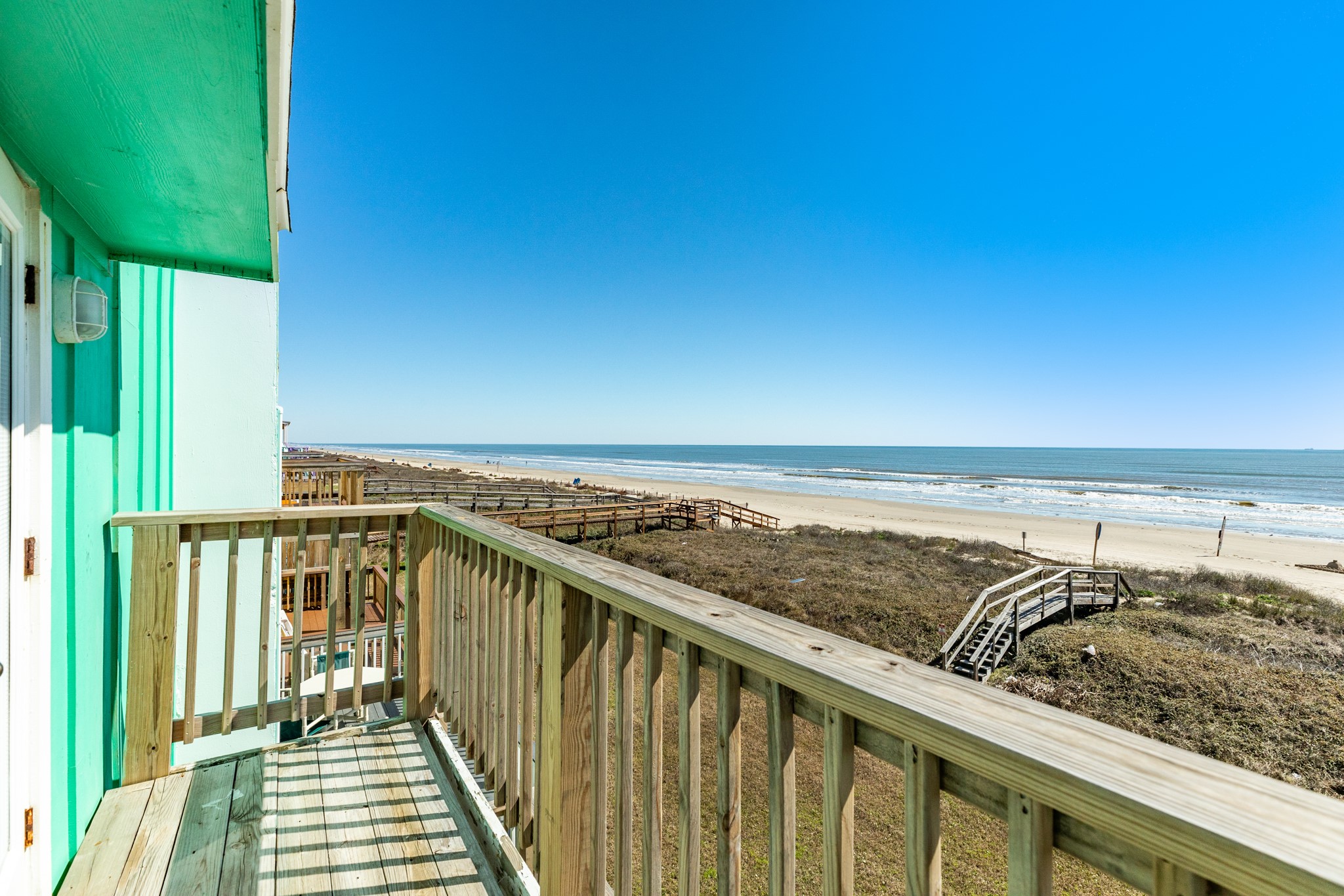 101 Pelican Place, Unit 7 Freeport, TX 77541 - Photo 32 of 44 This photo showcases a beachfront property with a wooden balcony offering stunning ocean views. The beach is accessible via a boardwalk, and the area is bathed in bright, natural light, perfect for enjoying coastal living.