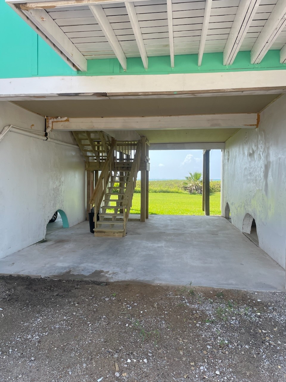 101 Pelican Place, Unit 7 Freeport, TX 77541 - Photo 40 of 44 This photo shows an elevated home's ground level with a concrete slab and wooden stairs leading up. It opens to a grassy area and offers potential for parking or storage.
