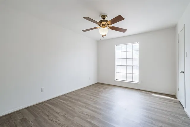 an empty room with wooden floor fan and windows