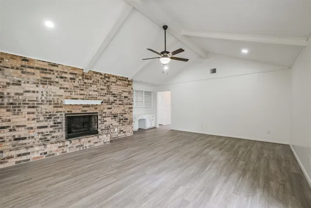 an empty room with wooden floor a ceiling fan a fireplace and windows