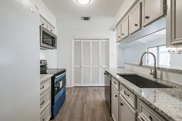 a kitchen with granite countertop a sink wooden floor and stainless steel appliances