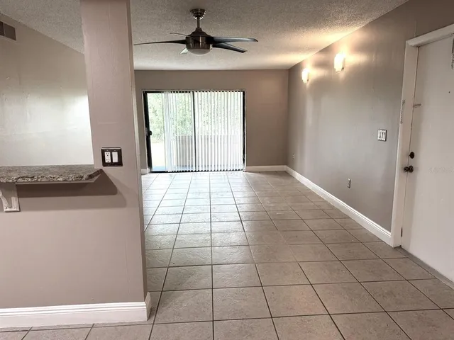 a view of an empty room with chandelier fan and kitchen view