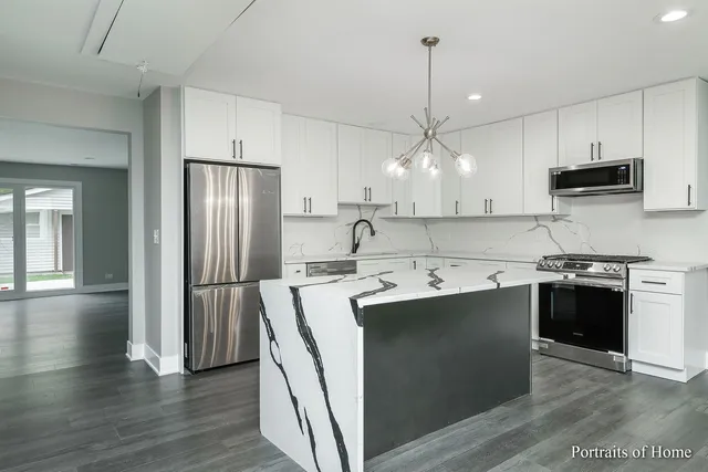 a kitchen with stainless steel appliances granite countertop a sink a stove a refrigerator and island with wooden floor