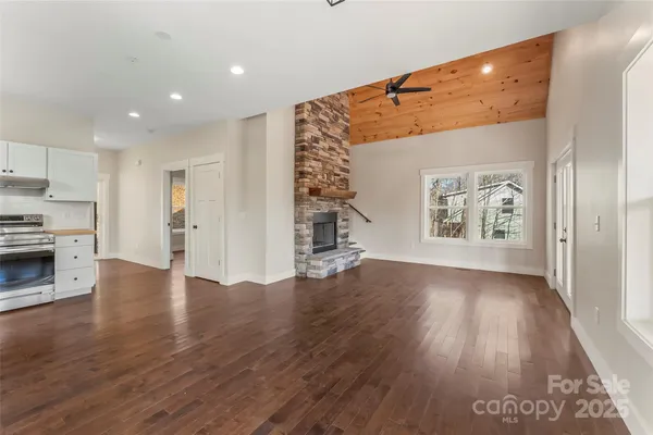a view of an empty room with wooden floor kitchen view and a window