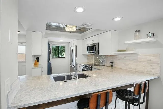 a kitchen with stainless steel appliances granite countertop a sink dishwasher a microwave oven a stove with white cabinets and wooden floor