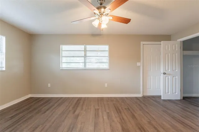 an empty room with wooden floor chandelier fan and windows