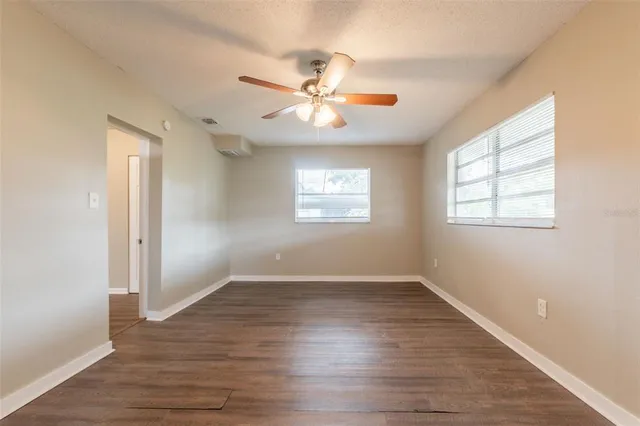 an empty room with wooden floor ceiling fan and windows