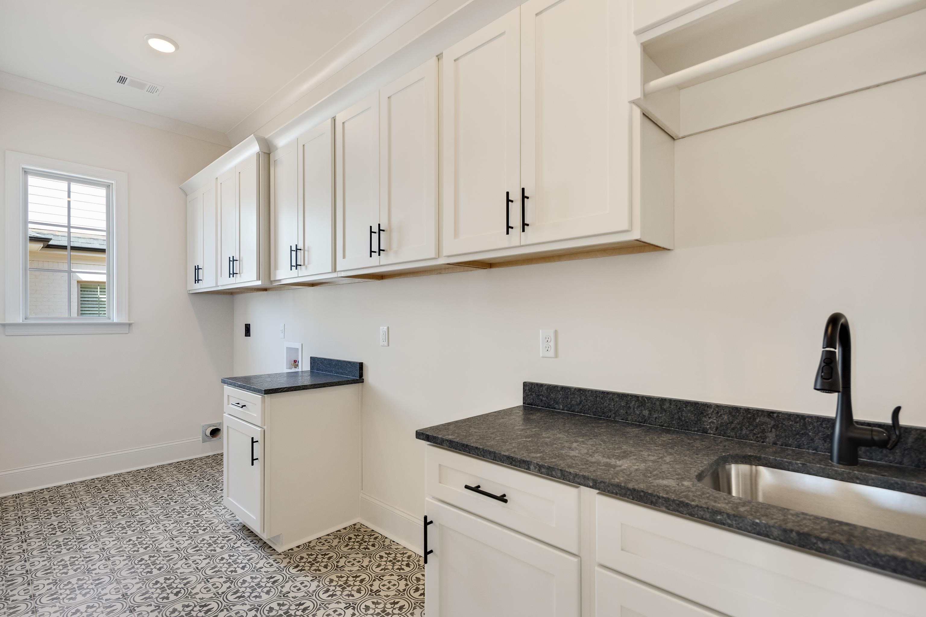 284 Keisie Lane Collierville, TN 38017 - Photo 19 of 34 Utility room featuring white shaker-style cabinetry with matte black hardware, dark stone countertops, a stainless steel sink with a black faucet, and patterned floor tiling