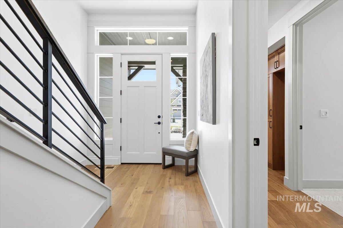 6762 South Messner Way Meridian, ID 83642 - Photo 2 of 35 Entryway featuring a white paneled door with glass inserts and transom windows, light wood-finish flooring, and a contemporary black metal baluster railing