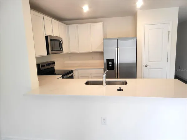 a large white kitchen with stainless steel appliances a refrigerator a stove a microwave and cabinets