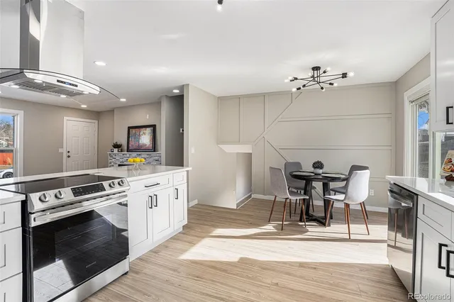 a open kitchen with stainless steel appliances granite countertop a stove top oven a dining table and chairs with wooden floor