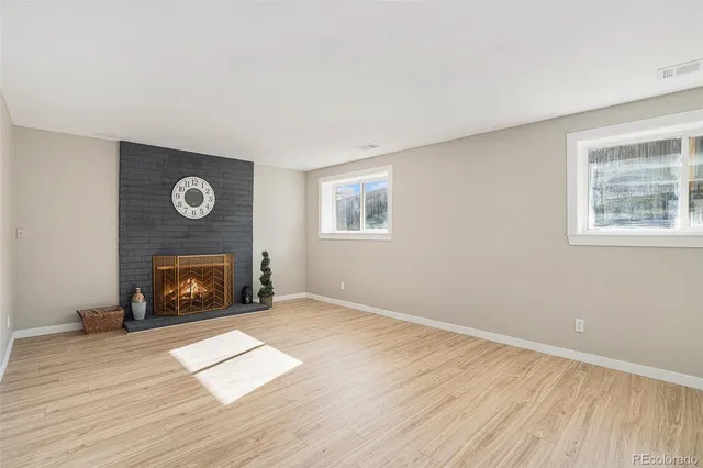 a view of an empty room with wooden floor fireplace and a window