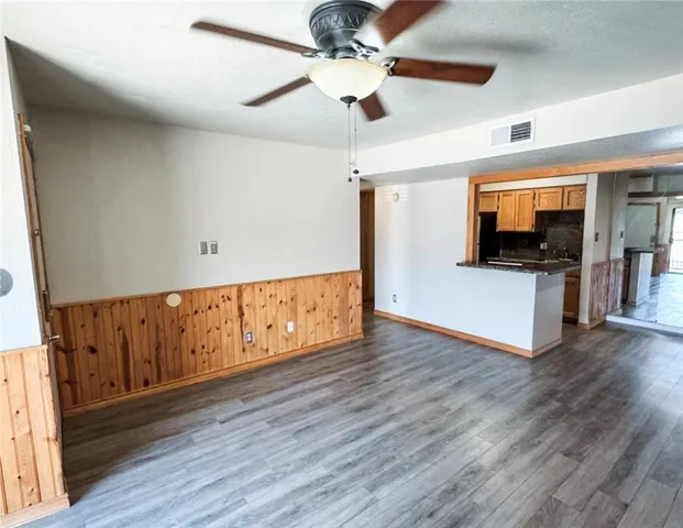 a view of an empty room with wooden floor and a kitchen