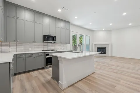 a kitchen with kitchen island granite countertop a stove top oven a sink dishwasher and a fireplace with wooden floor