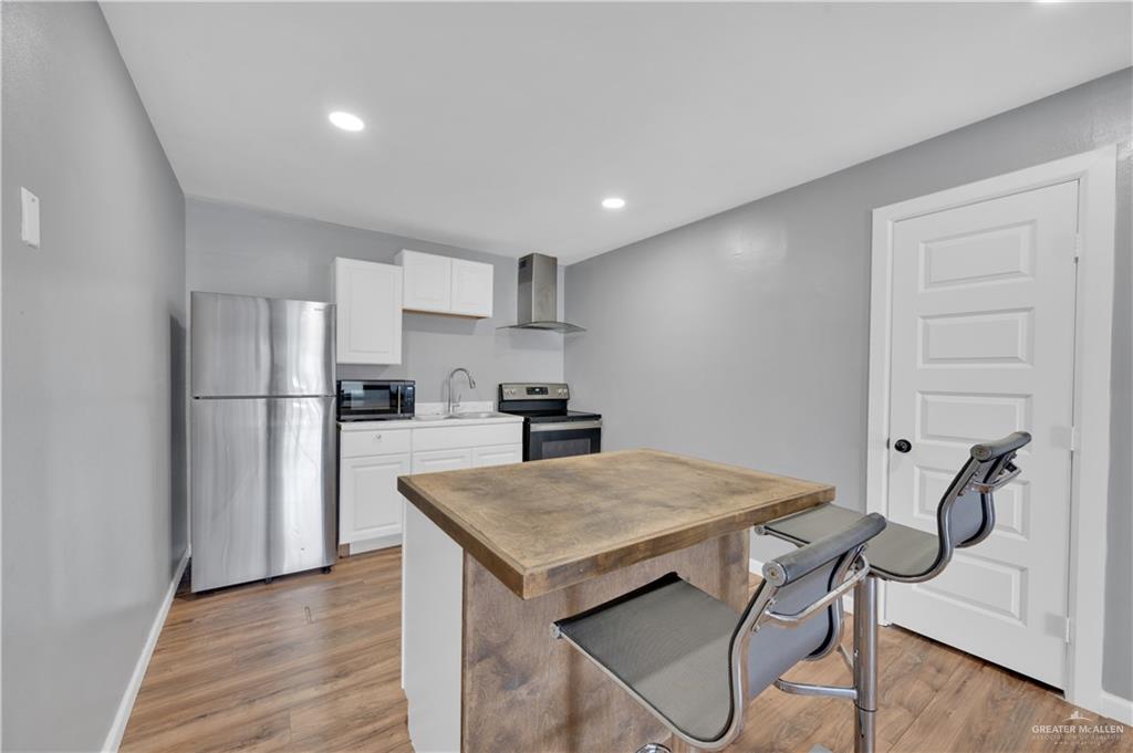 405 East Guerra Street Rio Grande City, TX 78582 - Photo 6 of 33 Kitchen featuring stainless steel appliances, wall chimney range hood, a sink, light wood-type flooring, and white cabinetry