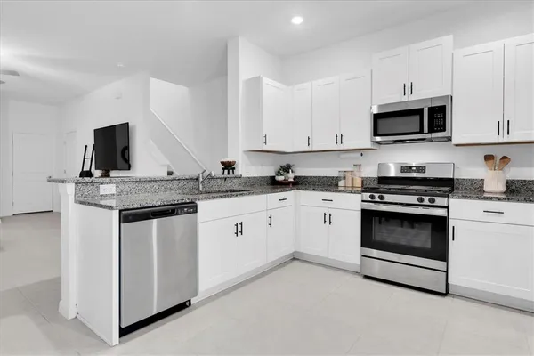 a kitchen with stainless steel appliances granite countertop white cabinets a refrigerator a stove a sink and dishwasher with wooden floor