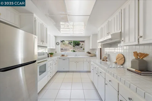 a kitchen with stainless steel appliances kitchen island granite countertop a refrigerator a stove and white cabinets