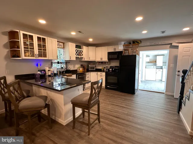 a kitchen with stainless steel appliances kitchen island granite countertop a refrigerator a stove a sink a dining table and chairs with wooden floor