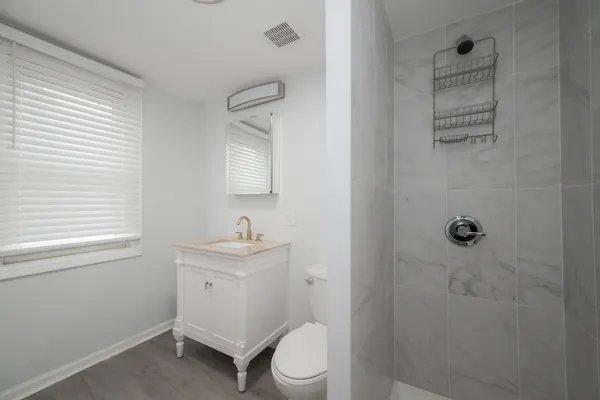 a bathroom with a granite countertop toilet a sink a shower and a window