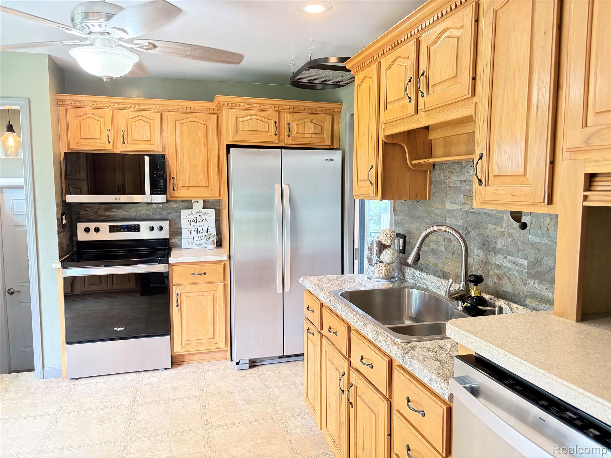 1451 Wilshire Road Haslett, MI 48840 - Photo 17 of 42 Kitchen featuring wood-finish cabinetry, stainless steel appliances, a double basin sink, and stone tile backsplash