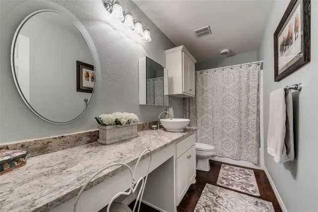 a bathroom with a granite countertop sink a toilet a mirror and shower