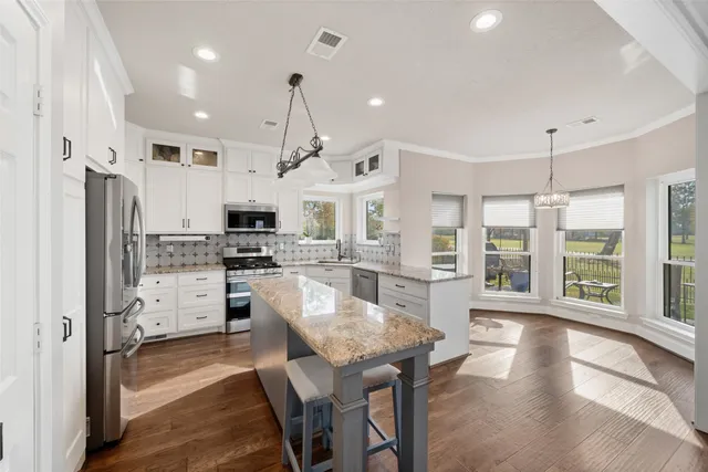 a kitchen with stainless steel appliances granite countertop a refrigerator a oven a sink a dining table and chairs with wooden floor