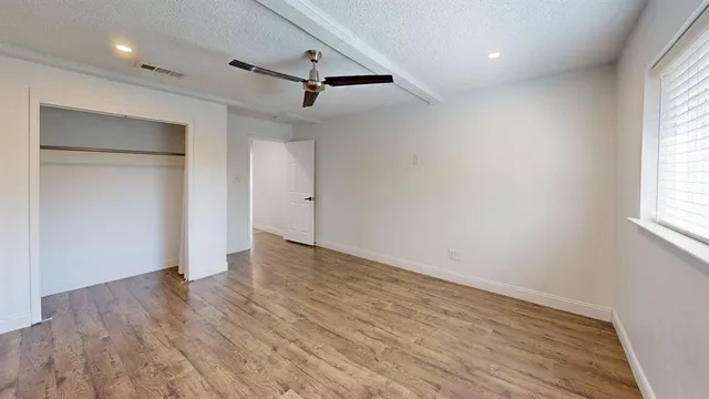an empty room with wooden floor a ceiling fan and windows