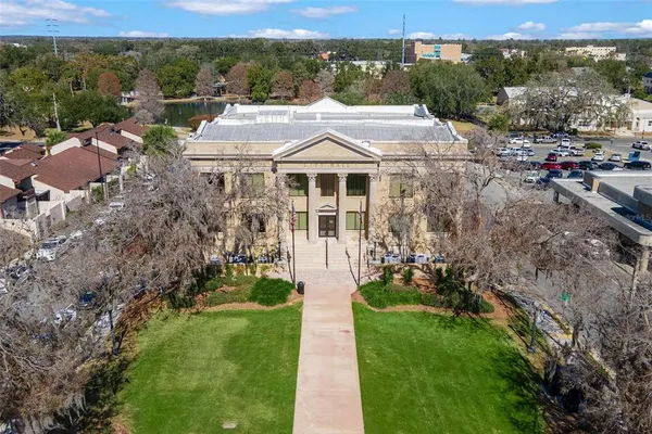 a view of a white house with a big yard plants and large trees
