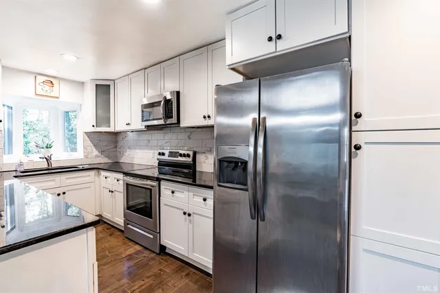 a kitchen with stainless steel appliances granite countertop a refrigerator a sink and white cabinets