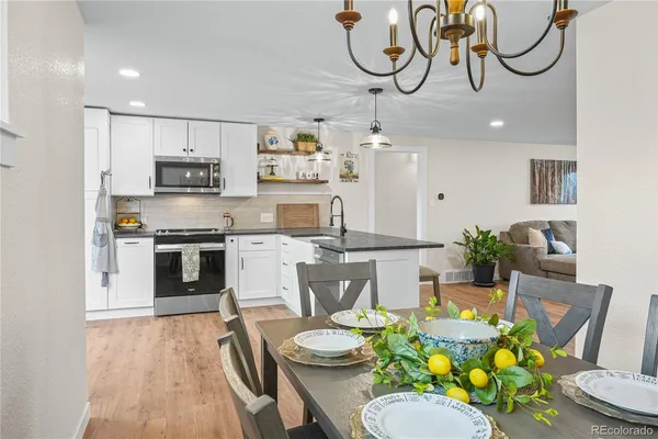 a kitchen with stainless steel appliances kitchen island granite countertop a sink a stove a dining table and chairs with wooden floor