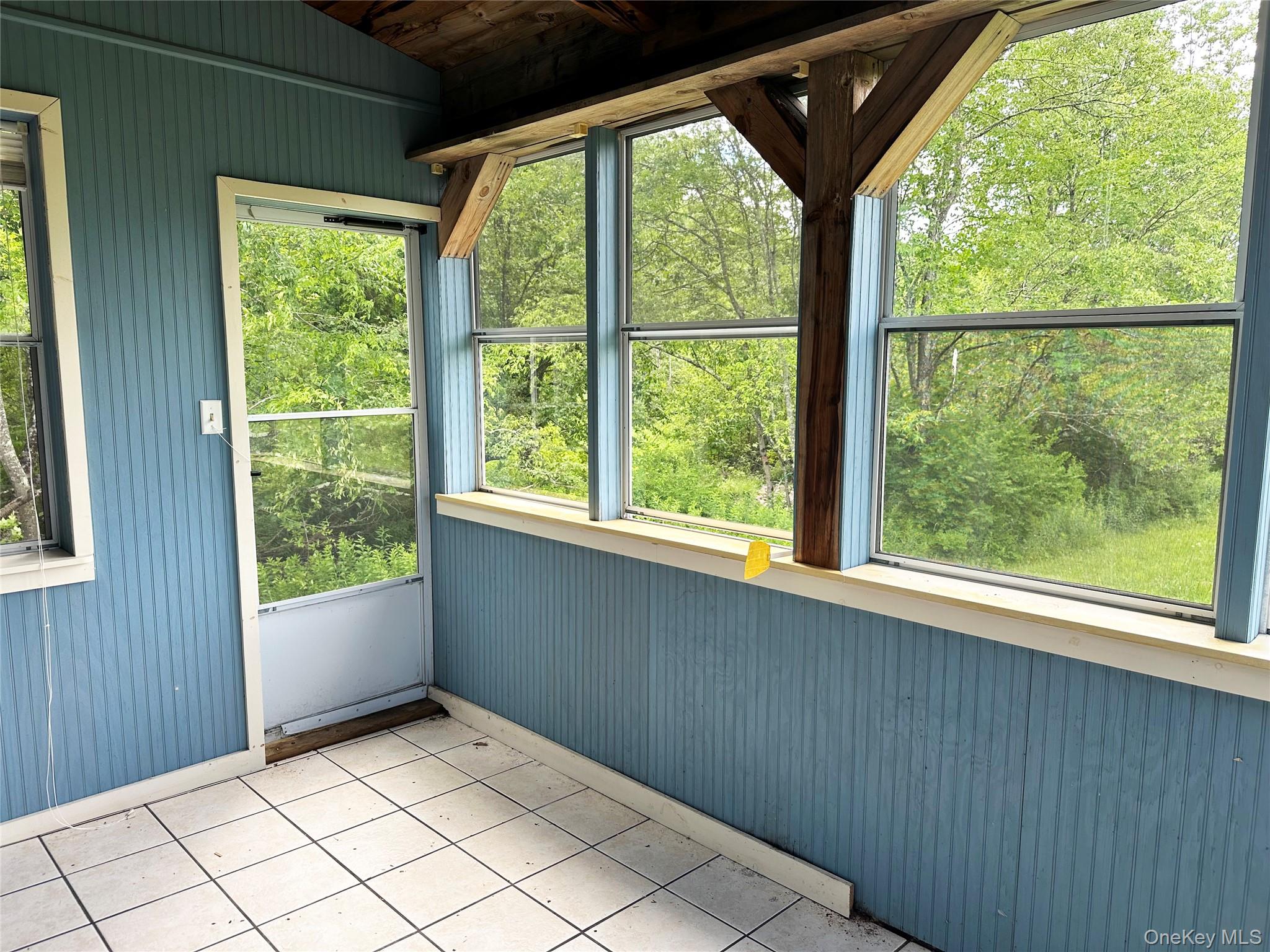 818 Methol Road Roscoe, NY 12776 - Photo 28 of 39 Enclosed sun room with exposed beams, panoramic woodland views, and direct outdoor access overlooking the natural landscape.