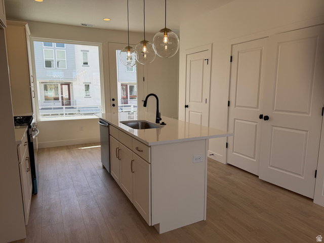 10995 South Freestone Road, Unit 109 South Jordan, UT 84009 - Photo 9 of 20 Kitchen with a center island with sink, light wood-type flooring, hanging light fixtures, stainless steel range with gas cooktop, and light stone counters