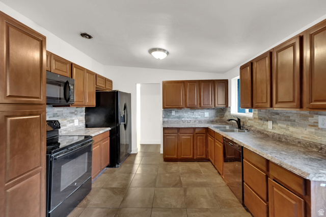 360 400 North Centerville, UT 84014 - Photo 13 of 30 U-shaped kitchen featuring wood cabinetry, integrated black appliances, stone-look countertops, and a full-height tile backsplash